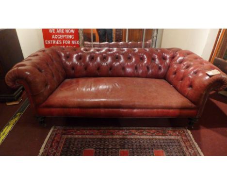 A Victorian Chesterfield sofa upholstered in buttoned burgundy leather and raised on turned ebonised supports and castors 