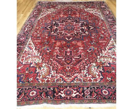 A large Persian Heriz carpet, decorated with a star medallion on a red field with spandrels, one Frieze and two running borde