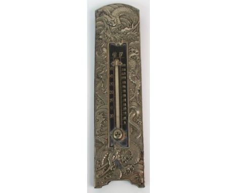 A Chinese white metal thermometer cast with dragons amongst crashing waves, enclosing a hardwood temperature scale, 23cm high