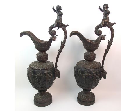 A large pair of bronze ornamental jugs with moulded scenes of putti sitting by a fire, upon a goat pulled carriage etc, the h