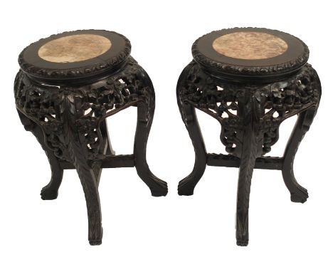 A pair of Chinese hardwood plant pedestals with marble inserts above foliate carved aprons on four scroll legs, 46cm high (2)