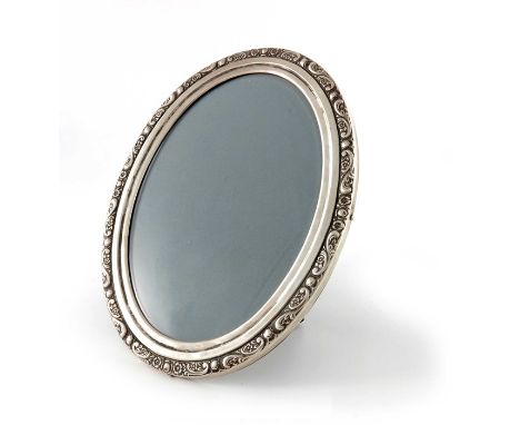 An early 20th century silver photo frame, oval form, embossed with foliate scrolls and rosettes to the stepped rim, wooden ea