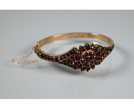 A Victorian garnet-set bangle, the oval half-hinged yellow metal bangle with central flower motif, concealed clasp, safety ch