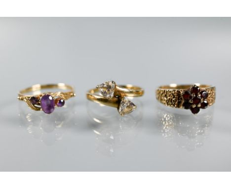 Three 9ct yellow gold rings - a three-stone amethyst in scroll setting, garnet cluster and two stone crossover ring, size N-O