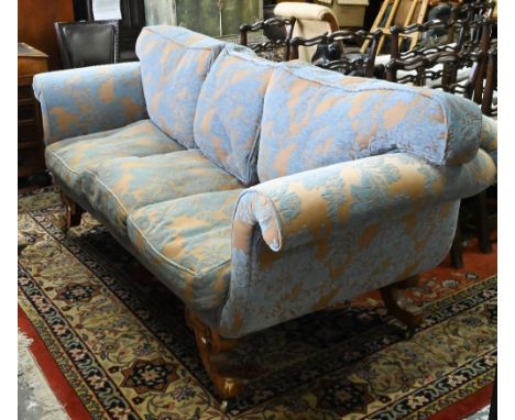 An walnut and upholstered three-seat sofa with blue and brown/gold upholstery / cushions, raised on out-swept legs to castors