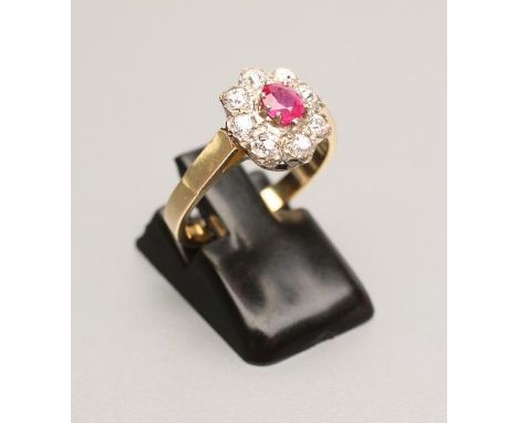A RUBY AND DIAMOND CLUSTER RING, the oval facet cut ruby claw set to a border of eight round brilliant cut diamonds to a plai