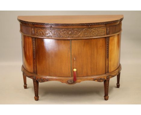 A GEORGIAN STYLE MAHOGANY COMMODE, 20th century, of demi lune form, the top with carved edge over baize lined slide, fluted f