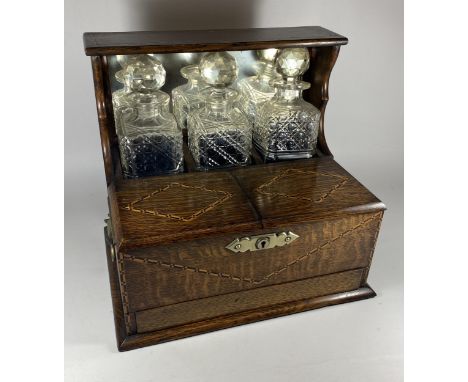 AN EDWARDIAN INLAID OAK THREE BOTTLE TANTALUS HOLDER WITH TWIN LIDDED COMPARTMENT AND LOWER DRAWER WITH CARDS AND CRIBBAGE BO