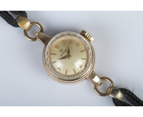 A ladies 9ct gold cased Omega manual wind wristwatch, on black rope strap. The champagne dial featuring baton markers, having
