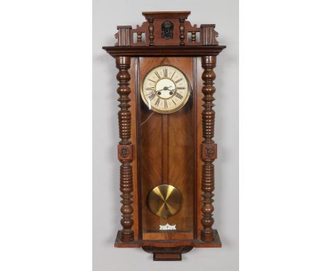 A large antique Vienna wall clock, with round decorated metal dial bearing Roman numerals, housed in a walnut case flanked by