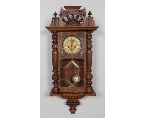 An antique walnut cased Vienna wall clock, featuring carved scrolls, foliage motifs and fluted columns, round metal dial with