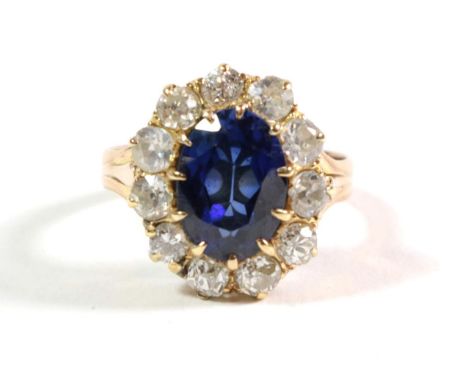 A synthetic sapphire and diamond cluster ring, an oval cut synthetic sapphire in a claw setting, within a border of old cut d