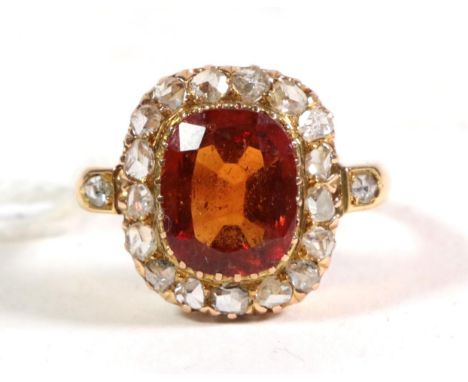 An 18 carat gold hessonite garnet and diamond cluster ring, a cushion cut hessonite garnet in a collet setting, within a bord