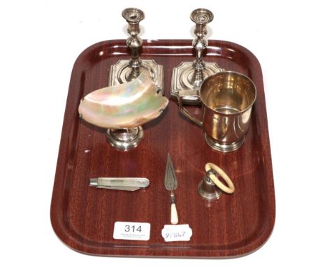 A silver christening mug, a pair of loaded candlesticks (a.f.), a silver mounted mother of pearl salt, a Victorian silver and