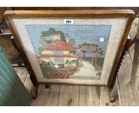 A vintage stained beech metamorphic fire screen/tea table with polychrome woolwork panel, depicting a cottage (under glass), 