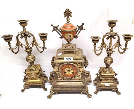 A late 19th Century ornate brass clock garniture comprising a clock with painted portrait to the ceramic urn finial and decor