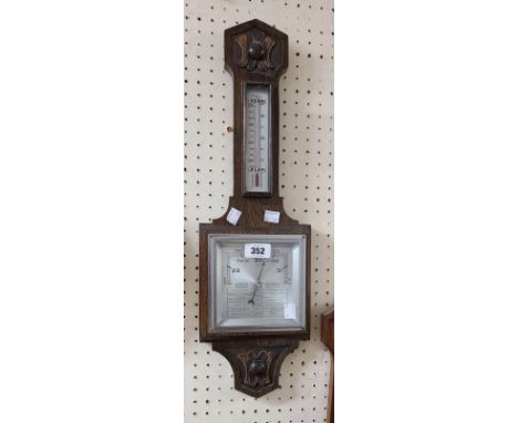 A small 1950's stained oak framed wall barometer/thermometer with printed detail to the square dial with aneroid works