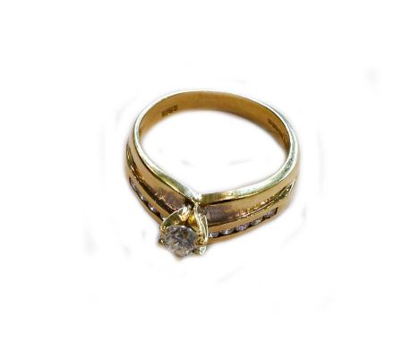 An 18 carat gold diamond ring, the raised round brilliant cut diamond in a yellow claw setting, flanked by a row of round bri