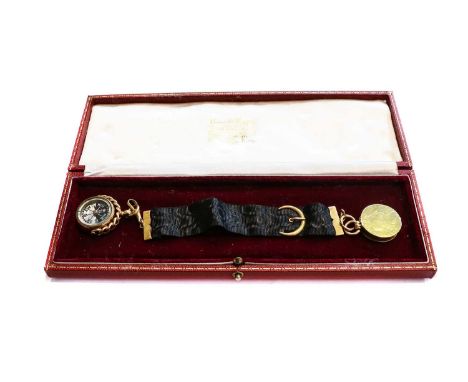 A coin locket suspended from a black ribbon with yellow detailing, stamped '9CT'; and a compass fob, stamped '18CT'Locket and