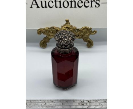 A Victorian ruby cut glass perfume bottle designed with an ornate silver [unmarked] top. Finished with original stopper. [9cm