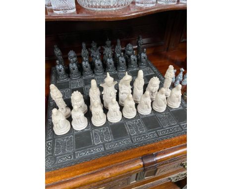 A Heavy hand carved slate chess board together with a set of oriental chess pieces made from resin. 