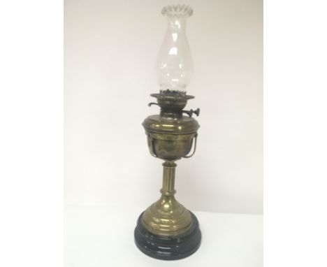 A Victorian brass oil lamp with glass chimney on a black ceramic base height 59cm.