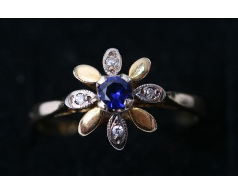 An 18ct yellow gold ring inset with a central sapphire and a floral shaped outer alternating with gold and white stones, appr