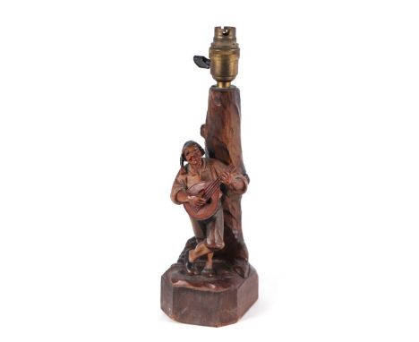 A Black Forest / Anri figural table lamp depicting a musician leaning against a tree, 32cms high.