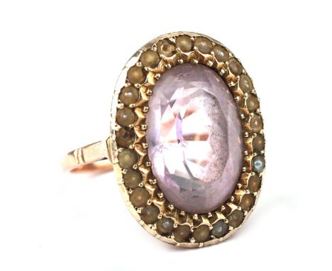 A late 19th century 9ct gold ring set with a large oval pale amethyst within a seed pearl border, approx UK size 'K', 5.6g.Co