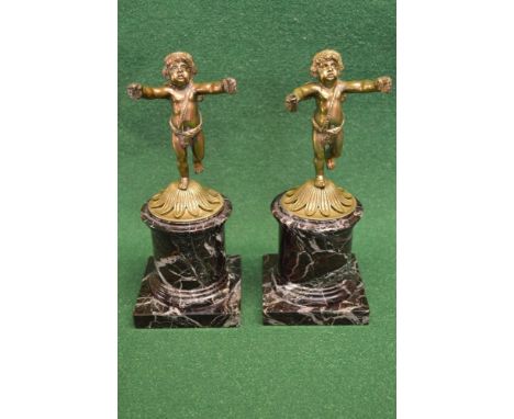 Pair of bronze cherub mantle garnitures each cherubs standing on circular leaf formed base supported on marble columns and sq