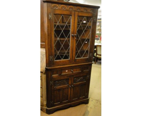 A reproduction oak 2-section corner cabinet, the top fitted with 2 lead light glazed doors with carved cupboards under on bra