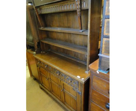 An oak dresser with a panelled open plate rack, the base fitted with carved drawers and panelled cupboards on bracket feet.