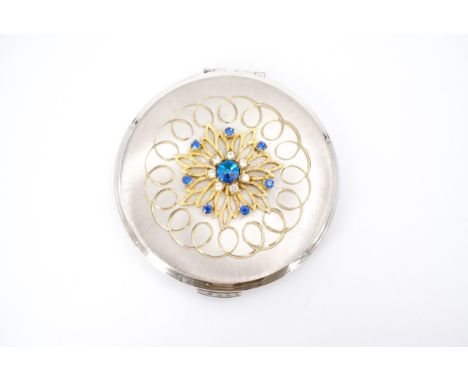 A Kigu powder compact, radially brushed, guilloche engraved and faced with a jeweled gilt stylized flowerhead ornament, circa