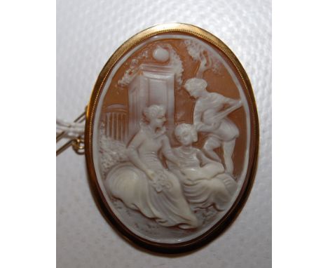 AN OVAL SHELL CAMEO DEPICTING A PASTORAL SCENE, YELLOW MOUNT TO A PIN AND ROLLER CATCH FITTING WITH HINGED PENDANT LOOP TO TO