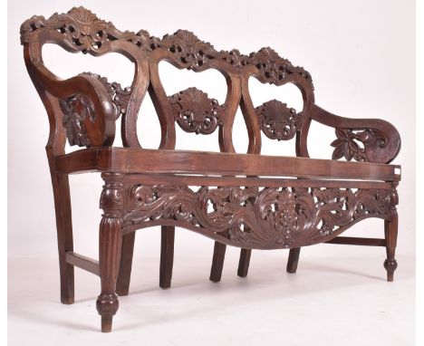 An Indo - Portuguese manner hardwood and cane hall bench. The bench having a carved pierced back rest with scrolled foliate m