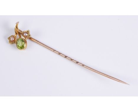 An antique 15ct gold, peridot and seed pearl stick pin: the flower shaped head set with an oval cut peridot and two seed pear