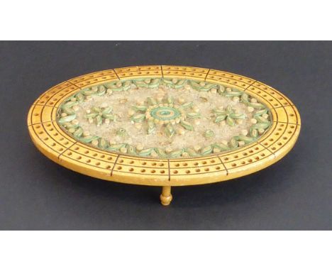 An unusual 19th century oval sycamore and rolled paper scroll cribbage board: central flower designs and raised on four turne