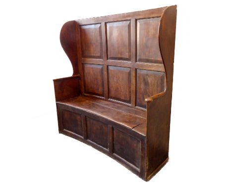 A concave panel back elm settle (18th/19th century): six fielded panels flanked by wings and above a concave hinged, lidded c