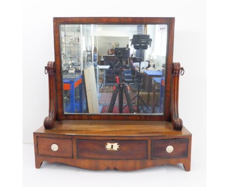 An early 19th century bow-fronted mahogany toilet mirror: the rectangular plate flanked by scrolling verticals and the base w