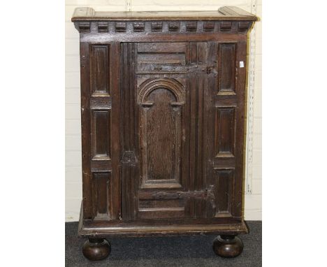 A 17th century and later oak cupboard, the block and moulded cornice above an arch panel door with iron strap hinges, flanked