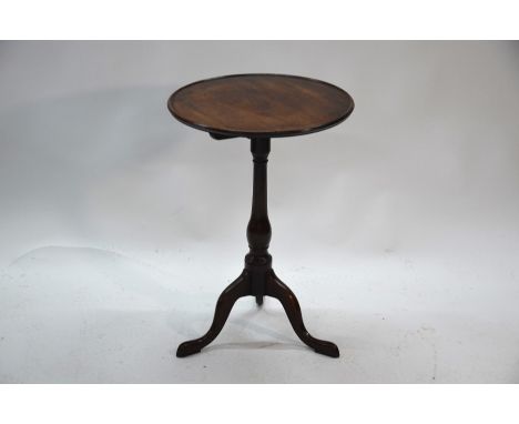 A George III mahogany tilt top wine table, the circular top with lipped edge raised on a vase turned column to swept legs, 50