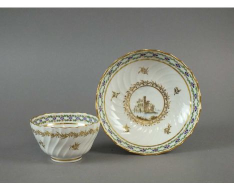 A Caughley tea bowl and saucer circa 1790-92 of wrythen moulded form and decorated with gilt wreaths enclosing enamelled vign