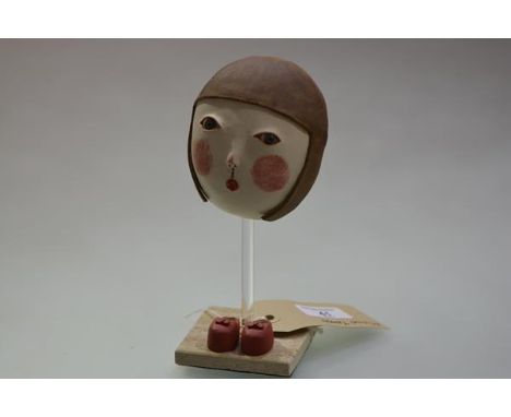 Midori Takaki (Contemporary), Ceramic Mask with Red Shoes, on a travertine stand. Height overall 19.5cm