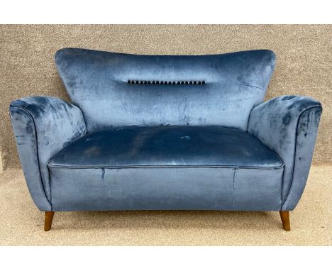 A mid-century blue brushed velvet two seater sofa having a flared back with a row of black buttons flanked by two curved and 