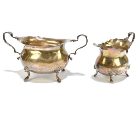 A George V hallmarked silver twin handled sugar bowl raised on four scrolling supports with a matching milk jug, Birmingham 1