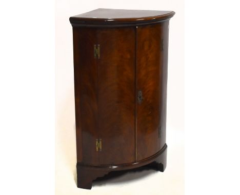 A 19th century mahogany freestanding bowfront corner cupboard, with twin panelled doors enclosing three fixed shelves, raised