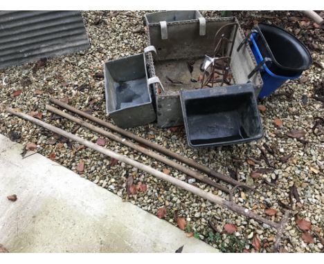 A square section horse trough with various additional metal and plastic hanging troughs, a pair of saddle racks and three han