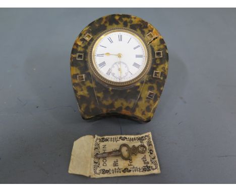 A horseshoe shaped tortoiseshell cased travel clock, Roman numerals to white enamel dial with subsidiary second hand at 6 o'c