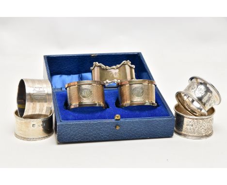A PAIR OF CASED GEORGE V SILVER CIRCULAR NAPKIN RINGS AND FIVE OTHER SILVER NAPKIN RINGS, the cased pair engine turned and en