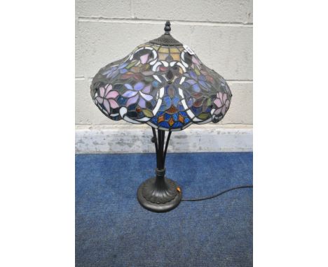 A TIFFANY STYLE TABLE LAMP, the shade with foliate details, of various colours, raised on a shaped support, with a stepped ba